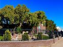 Brick home showcasing beautiful landscaping, mature trees, and elegant wrought iron fencing with brick columns at 8690 W Ford Ave, Las Vegas, NV 89148