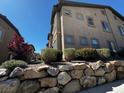 Exterior view of a tan condo building featuring well-maintained landscaping and a sturdy rock wall at 8985 S Durango Dr # 1010, Las Vegas, NV 89113