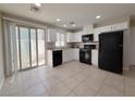 Well-lit kitchen featuring white cabinets, black appliances, tile floors, and sliding door to patio at 5271 Aurora Beam Ave, Las Vegas, NV 89122