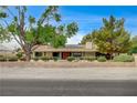Wide front view of the single story home with lush trees and a low brick fence at 3015 Duneville St, Las Vegas, NV 89146