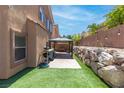 Private backyard featuring a stone retaining wall, artificial turf, and shaded patio with gazebo at 7641 Lani Dawn St, Las Vegas, NV 89149