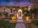 Charming stone entryway with an arched gate, lush greenery, and illuminated landscaping at 12056 Royal Dolnoch Ct, Las Vegas, NV 89141