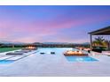 An expansive pool has built-in lounge chairs and fire features with views of mountains and city lights beyond at 34 Olympia Outlook Dr, Las Vegas, NV 89141