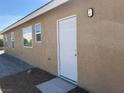 Exterior view of side of home with white door, two windows, and neutral stucco at 3016 Mount Charleston Dr, Pahrump, NV 89048