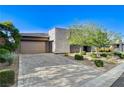 Modern home featuring a gray stone and stucco exterior, a paver driveway, and lush landscaping at 10004 Terrastone Dr, Las Vegas, NV 89148