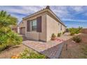 A tan one-story home is shown with a well-kept side yard and desert landscaping at 1108 Via Della Curia, Henderson, NV 89011