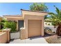 Close-up of a one-car garage with a gate, stucco wall, and mature plants at 2489 Black River Falls Dr, Henderson, NV 89044