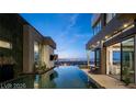 Side view of luxurious backyard featuring infinity pool, outdoor seating, bar and city views at dusk at 1491 Reims Dr, Henderson, NV 89012