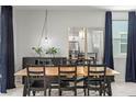 Bright dining room with modern light fixture, wood table and large windows with dark curtains at 6848 Calvitero St, Las Vegas, NV 89149