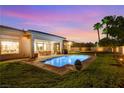 Backyard with sparkling pool, covered patio, well-manicured lawn, and lush landscaping under a sunset sky at 10969 Tranquil Waters Ct, Las Vegas, NV 89135
