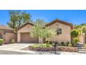 Tan single-story house with a brown garage door, well manicured yard and greenery at 35 Glade Water Dr, Henderson, NV 89052
