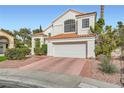 Inviting two-story home featuring a white stucco facade, clay tile roof, brick-patterned driveway, and tidy landscaping at 9921 Heffner Hills Cir, Las Vegas, NV 89117
