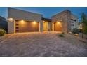 Modern home with a three-car garage, sleek design, stone accents, and an attractive paved driveway, enhanced by landscape lighting at 11954 Camden Ridge Ct, Las Vegas, NV 89138