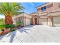 Close-up view of a three-car garage with lush landscaping and a charming arched entrance at 11275 Gammila Dr, Las Vegas, NV 89141