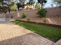 A spacious backyard with brick pavers, a small patch of grass, and tasteful landscaping along the retaining wall at 2947 Caxton Grove Dr, Henderson, NV 89052