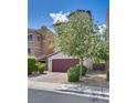 Stucco home with a driveway and a well-maintained lawn featuring flowering tree and manicured bushes at 345 Gracious Way, Henderson, NV 89011