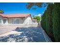 View of the side of the home featuring a terra cotta roof, stucco walls, and a tall green privacy hedge at 8340 W Fisher Ave, Las Vegas, NV 89149