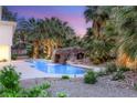 Backyard pool featuring a rock grotto waterfall, surrounded by palm trees, lush landscaping, and a tranquil setting at 7185 Ranchito Cir, Las Vegas, NV 89120