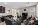 Cozy living room features tile floors, neutral walls, large windows, and comfortable, dark leather furniture at 7769 Peaceful Trellis Dr, Las Vegas, NV 89179
