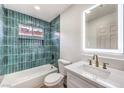 Bathroom featuring a tub with green tile surround, white vanity, and illuminated mirror at 2536 Herrod Dr, North Las Vegas, NV 89030