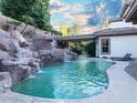 Inviting backyard swimming pool featuring a rock waterfall feature, seating area, and lush landscaping at 764 Ricota Ct, Henderson, NV 89012