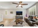 Bright living room with wood floors, a ceiling fan, plantation shutters, and a large television at 10565 Olinda St, Las Vegas, NV 89179
