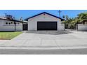 A detached garage with a black door, a white exterior, and a wide, spacious driveway at 819 Bracken Ave, Las Vegas, NV 89104