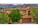 Attractive tan two-story home with a tiled roof, front balcony, mature landscaping, and mountain views at 617 Apricot Rose Pl, Las Vegas, NV 89138