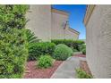 Exterior side view featuring a landscaped walkway, lush green bushes, and neutral exterior paint at 5373 Painted Mirage Rd, Las Vegas, NV 89149