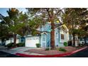 Attractive blue two-story townhome featuring a white garage door, neat landscaping, and mature trees at 3217 Symphony Dr, Las Vegas, NV 89146