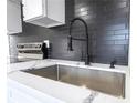 Close-up of the kitchen featuring stainless steel sink, faucet, and a sleek black tile backsplash at 266 Tungsten St, Henderson, NV 89015