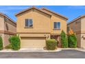 View of a tan two-story home showcasing a two-car garage and manicured bushes at 9457 Alma Ridge Ave, Las Vegas, NV 89178
