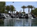 Picturesque pond with a tiered rock waterfall, mature trees, and tranquil water at 7957 Fantail Dr, North Las Vegas, NV 89084