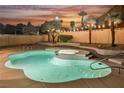 A kidney-shaped pool and hot tub are bordered by desert landscaping and string lights creating a relaxing backyard at 8401 Airmont Ct, Las Vegas, NV 89128