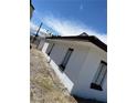Side view of a charming white house with brown trim, set against a bright blue sky and a gravel yard at 2417 St George St, North Las Vegas, NV 89030