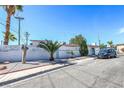 Exterior view of a well-maintained home featuring a white fence, palm trees, and a neatly paved sidewalk at 1521 Sombrero Dr, Las Vegas, NV 89169