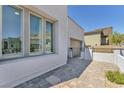 View of the side of a modern home showing a brick driveway, neutral stucco, and large window at 11707 Hatchling Ave, Las Vegas, NV 89138