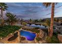 Backyard pool with tropical landscaping and a view of the lake at dusk creates a relaxing ambiance at 11359 Winter Cottage Pl, Las Vegas, NV 89135