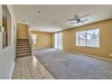 Spacious living room featuring neutral carpeting, a ceiling fan, staircase, and natural light streaming through large windows at 6381 Pronghorn Ridge Ave, Las Vegas, NV 89122