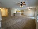 Open-concept living room with neutral paint, carpet, and ceiling fans, flowing into the kitchen area at 2224 Waterton Rivers Dr, Henderson, NV 89044