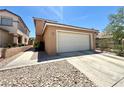 Beige home featuring a large, two-car garage and a concrete driveway with rock landscaping under a bright blue sky at 6287 Stone Hollow Ave, Las Vegas, NV 89156