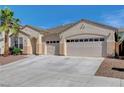 Beige single story home with a three car garage, landscaped yard, and palm tree under a clear, blue sky at 981 Buffalo River Ave, Henderson, NV 89002