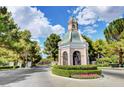 Picturesque neighborhood entrance with clocktower, manicured hedges, and colorful flowers at 9704 Royal Lamb Dr, Las Vegas, NV 89145