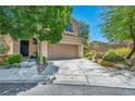 Inviting front yard with lush landscaping, mature trees, and a wide driveway leading to an attached two-car garage at 10692 Tulip Valley Rd, Las Vegas, NV 89179