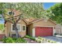 Beautiful home featuring a red garage door, mature trees, and meticulously maintained landscaping at 9370 Corkfish St, Las Vegas, NV 89178