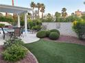 Landscaped backyard featuring a sparkling pool, covered patio, lush greenery, brick privacy wall, and plenty of room to relax at 2440 Ping Dr, Henderson, NV 89074