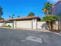 Attached two-car garage with white door, brick trim, and red tile roof, nestled among palm trees and white brick walls at 2104 Plaza De La Candela, Las Vegas, NV 89102