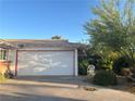 Two-car garage with adjacent landscaping featuring a desert tree and patio chair on a concrete driveway at 3382 Berwyck St, Las Vegas, NV 89121