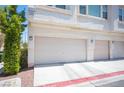 Three-car garage featuring tan doors, and exterior wall lighting with exterior landscaping at 9322 Straw Hays St # 103, Las Vegas, NV 89178