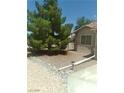 View of the side yard featuring drought-resistant landscaping, a mature tree, and gated access at 1611 Red Rock Dr, Pahrump, NV 89048